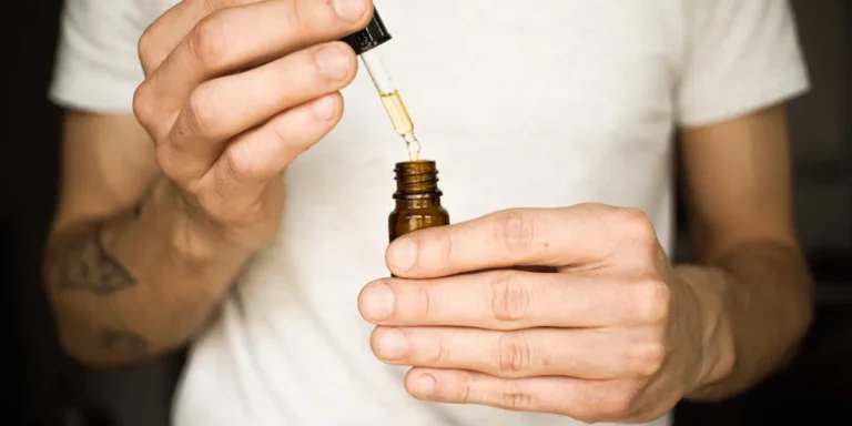 CBD Öl Tropfen unter der Zunge, Fläschchen mit Pipette in der Hand